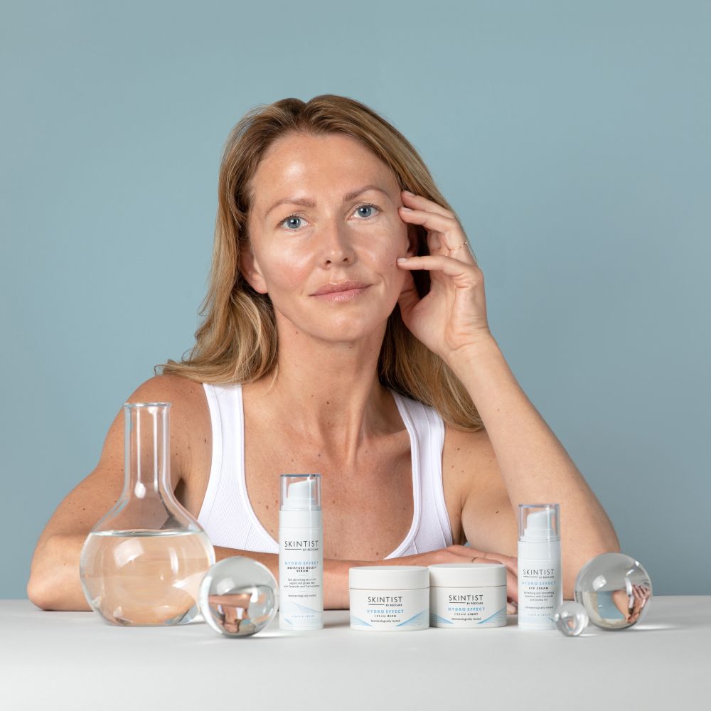 Frau mit Produkten auf dem Tisch. Produkte: SKINTIST HYDRO EFFECT Serum und Creme.